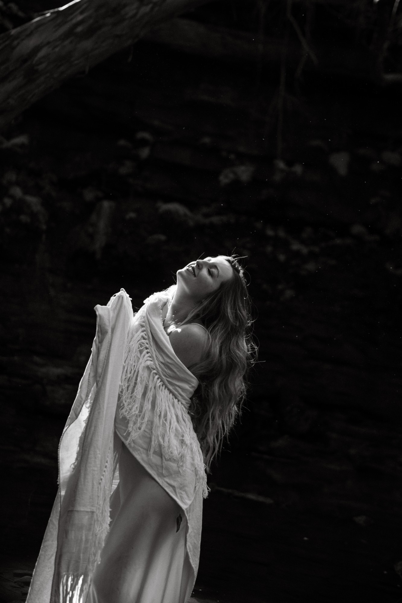 Louisa wrapped in a fringed shawl, head tilted back and smiling, in light against dark sandstone