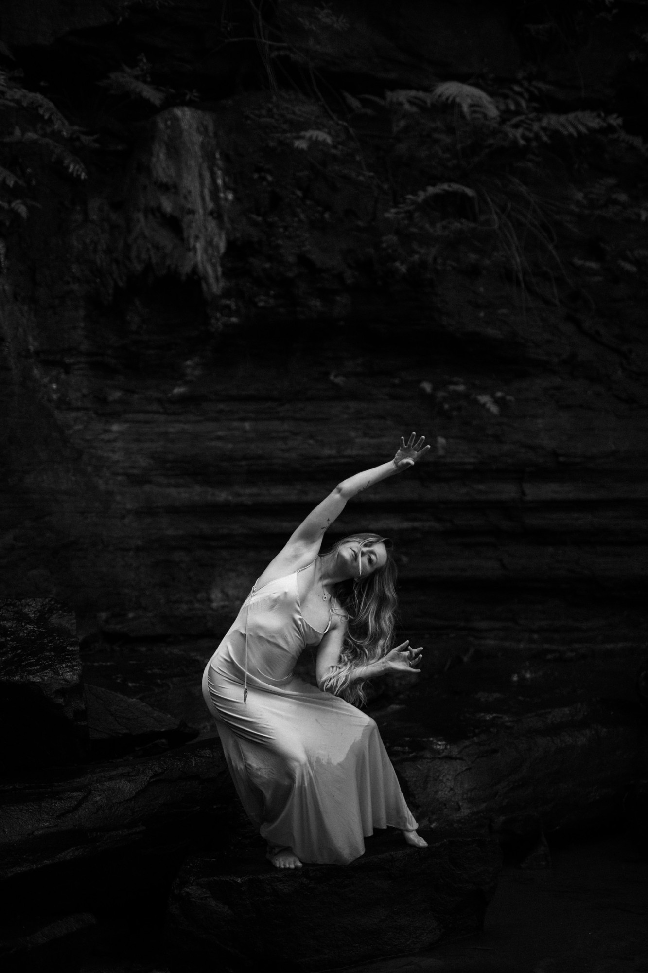Louisa moving freely in a white dress against dark sandstone, one arm reaching skyward