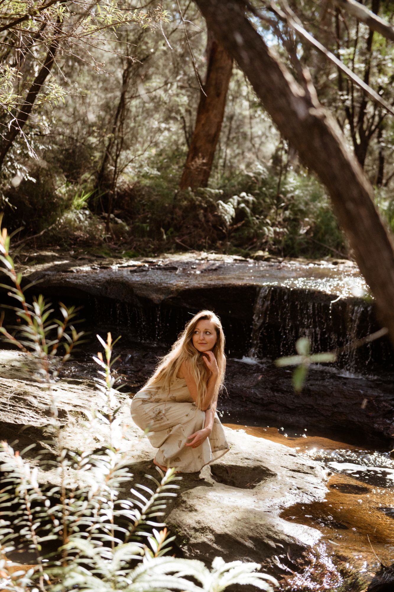 Louisa crouching beside a waterfall in the bush