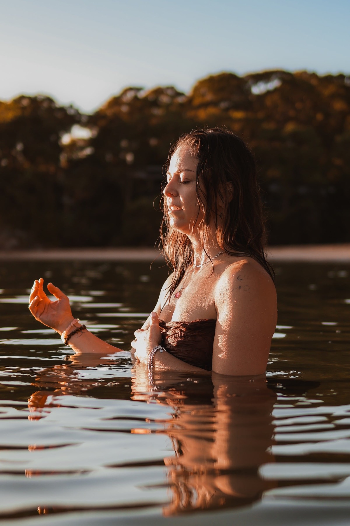 A woman standing in still water at dusk, holding a flower